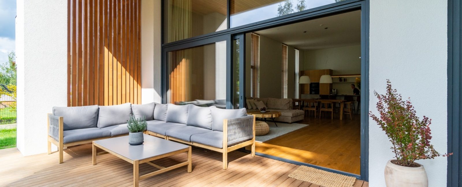 Wooden patio connected to a private building, with seating area and cozy lounge zone, open window with entrance to the house.